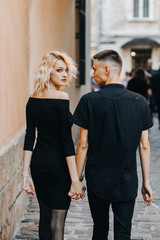 Fashionable couple walking down the street holding hands. Gorgeous blonde woman looking back