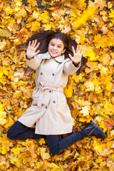 Young beautiful little girl in beige coat lying on yellow leaves