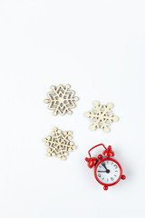 Simple Christmas composition. Small analog red clock, wooden snowflakes on white background. Minimal style flat lay, for social media. Top view. Celebration concept