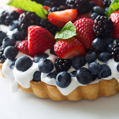 Top view of a colorful mixed berry tart with fresh whipped cream and mint garnish. 