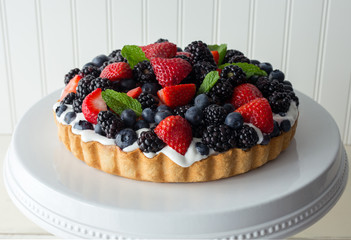 Top view of a whole mixed berry tart with fresh whipped cream and mint garnish. 