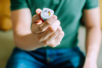 A young man is holding an asthma inhaler device while sitting on a couch