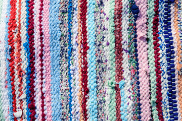 Fototapeta premium Background of manually woven textile materials of different colours, red, green, yellow, blue, green and pink pieces, with vertical lines, photographed with soft focus