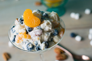 Close up of a serving of ambrosia fruit salad in a martini glass, topped with a mandarin orange slice. 