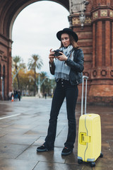 Photographer tourist with retro photo camera. Young girl in hat travels in Triumphal arch Barcelona. Holiday concept street in europe city. Traveler hipster shoot architecture, copy space mockup