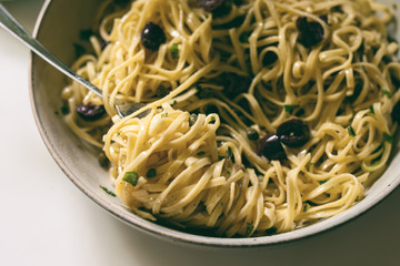 Close up view of a nest of linguine with basil, garlic, black olives, capers and olive oil. 