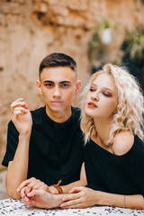 Portrait of a girl sitting at a table and inhaling smoke from her boyfriend's cigarette