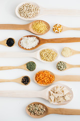mixed pulses in wooden spoon. rice, red lentils, green lentils, corn, bulgur, dried mint, isot, black pepper, oregano, pasta, wire noodle, scallops.