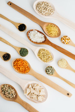mixed pulses in wooden spoon. rice, red lentils, green lentils, corn, bulgur, dried mint, isot, black pepper, oregano, pasta, wire noodle, scallops.