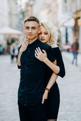 Cute blonde in a black dress hugging her boyfriend from behind