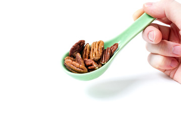 hand holding  green spoon with pecan nuts on white background