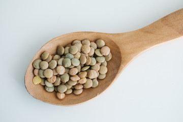 green lentil in a wooden spoon. on white background