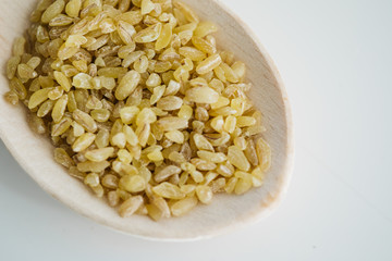 Bulgur grains in wooden spoon. On the white floor