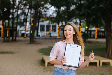 Young girl standing with visa application on resort, keeping pen.