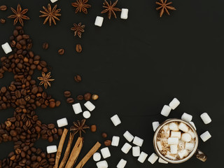 Coffee beans laid out in the shape of a Christmas tree on a black stone background. Cup of coffee with marshmallows, marshmallows and spices for the festive New Year drinks on the table. Top view