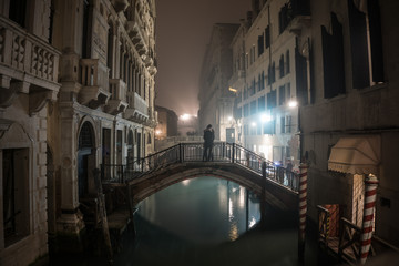 Lovers on a bridge at night in a foggy Venice