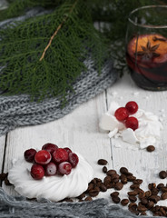 Meringue decorated with cranberries and coffee grains on a white wooden background. Glass with mulled wine and coniferous branches with decorations. New Year's breakfast concept