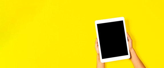 Kid hands holding white tablet computer on yellow background