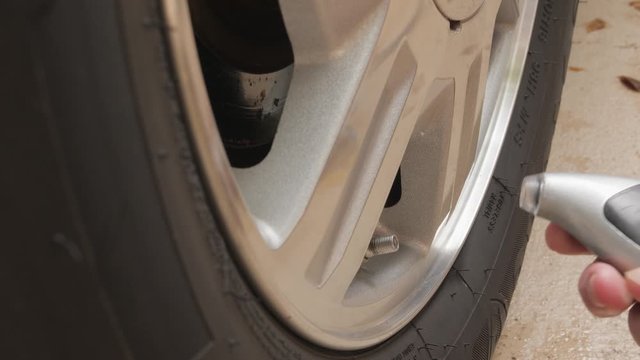Mechanic checking automotive tire for proper inflation. Man using digital air pressure gauge to check car tire air pressure.
