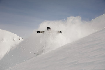 Snowboarder riding down the snow covered hill making a white splash