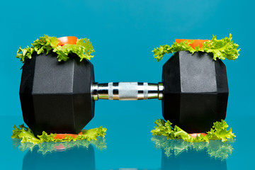 dumbbell with lettuce and chopped tomatoes on a blue background. The concept of eating iron,...