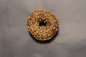 chocolate donut sprinkled with crushed nuts onblack background, top view