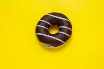 chocolate donut with white stripes on yellow background, top view