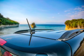 The roof of a dark car with space for your product. Cliff and ocean landscape with blue skies. Copy space. Sunny warm day. Summer time and car trip. © magdal3na