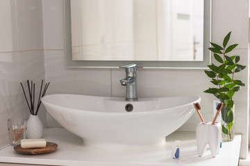 Bio-degradable, compostable bamboo toothbrushes in a tooth shape cup in a bathroom white interior. Green plant decor in background.