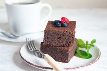 chocolate brownies cake decorated with mint and berries on a white plate