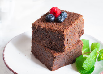 chocolate brownies cake decorated with mint and berries on a white plate