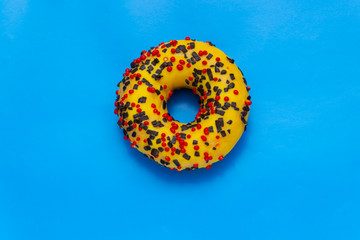 yellow donut with red and black powder on background, top view