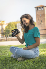 Photographer girl sitting on the grass looking at the camera screen, smiling, happy