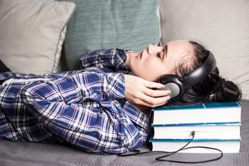 Weird strange, relaxed woman laid her head on the old thick books that she kind of listens through headphones with a wire and on her face is bliss and pleasure.