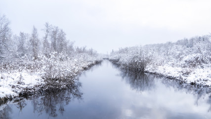 Winter landscape of a calm river and trees covered of first snow. Room for text. (copy space)
