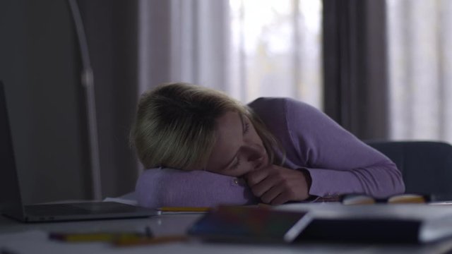 Blurred mobile phone ringing at the foreground as its owner sleeping at the background. Young blond Caucasian woman got asleep at the table in office. Overwork, hardworking.