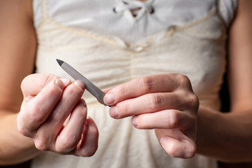Hands of a woman who does manicure for herself with the help of a metal nail file.
