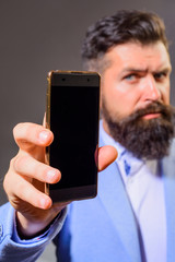 Businessman holds smartphone. Business, communication, internet, technology concept. Businessman show smart phone with blank screen. Business man shows mobile phone. Bearded man in suit showing phone.