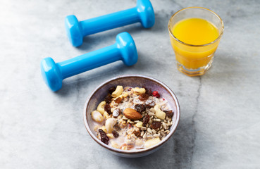 Bowl of granola with yogurt, nuts, raisins, cranberries and chia seeds. Blue dumbbells in background. Concept for a tasty and healthy meal. Stone background. Close up. 