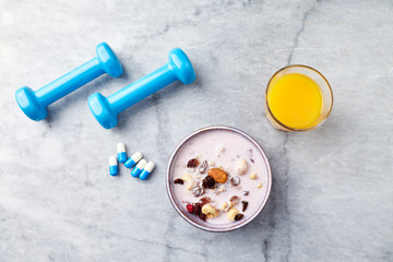 Bowl of granola with yogurt, nuts, raisins, cranberries and chia seeds. Blue dumbbells and sports supplements in background. Concept for a tasty and healthy meal. Stone background. Copy space