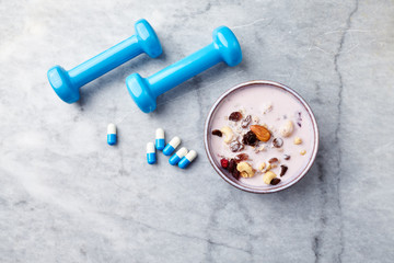 Bowl of granola with yogurt, nuts, raisins, cranberries and chia seeds. Blue dumbbells and sports supplements in background. Concept for a tasty and healthy meal. Stone background. Copy space