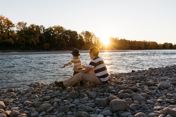 Father and son having fun by the river at sunset