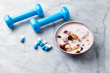 Bowl of granola with yogurt, nuts, raisins, cranberries and chia seeds. Blue dumbbells and sports supplements in background. Concept for a tasty and healthy meal. Stone background. Copy space