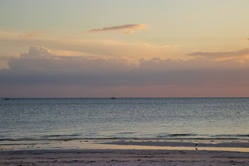 Cumulus clouds during colorful sunset with speedboats in distance on Gulf of Mexico