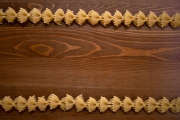 Two lines of pasta bows on a wooden background.