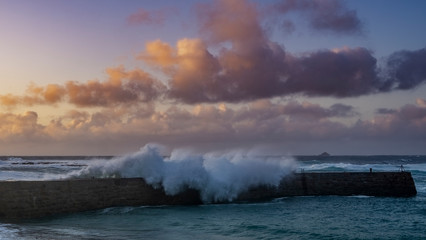 Fototapeta na wymiar As the sunsets waves crash onto Rocks near Sennen Harbour, Atlantic Ocean Cornwall West Country England UK United Kingdom GB