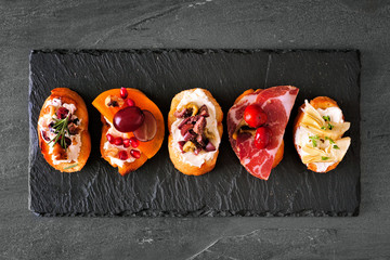 Mixed crostini appetizers with a variety of toppings. Top view on a dark slate background. Party...