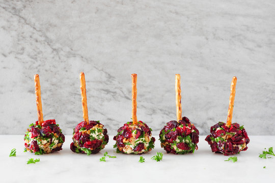 Christmas cheese ball appetizers with cranberries, pecans and herbs in a row on a white stone background.