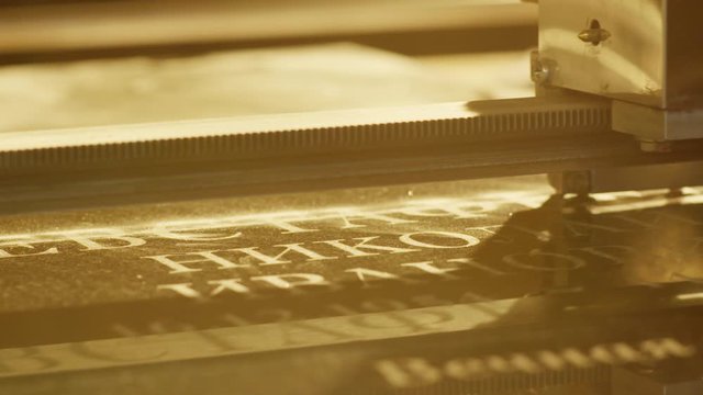 Closeup view of automated carving machine working and engraving letters and patterns on surface of dark granite block dedicated for memorial stones or headstone.