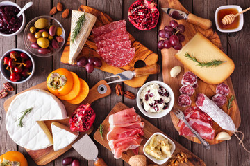 Charcuterie boards of assorted cheeses, meats and appetizers. Above view table scene on a rustic wood background.